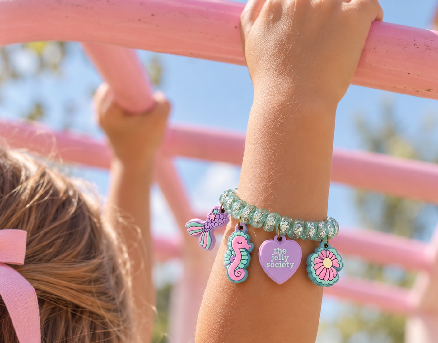 Child reaching up on pink monkey bars wearing a jelly charm bracelet